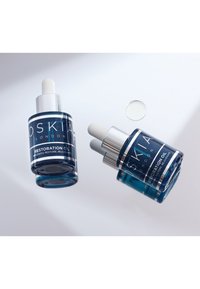 Två blå glasflaskor med Oskia Restoration Oil, med vita pipetter, silverdetaljer och svarta etiketter som visar produktinformation.