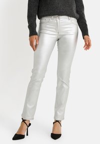 Jean métallisé argenté à coupe slim, doté de cinq poches, d'une braguette à fermeture éclair et de coutures dor ées, assorti à des chaussures à talons hauts noires.