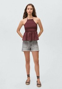 Burgundska peplum majica s smockanim topom, kombinirana s sivim razderanim trapericama. Model nosi smeđe espadrile s remenčićima oko gležnjeva.
