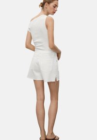 Un haut sans manches blanc associé à un short en denim blanc, avec un ourlet effiloché et des fentes sur les côtés, complété par des sandales simples.