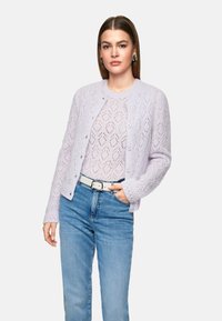 Lila gestrickte Strickjacke mit einem Blattmuster, Rundhalsausschnitt, Knopfverschluss und langen Ärmeln, kombiniert mit hellblauen Jeans und einem weißen Gürtel.