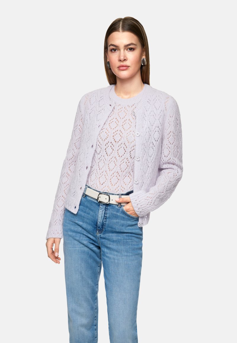 Lila gestrickte Strickjacke mit einem Blattmuster, Rundhalsausschnitt, Knopfverschluss und langen Ärmeln, kombiniert mit hellblauen Jeans und einem weißen Gürtel.