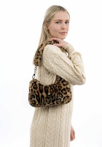 Pūku leopardu raksta rokas soma, izgatavota no mīksta mākslīgā kažokāda, ar izliekta formas dizainu, zelta ķēdes siksnu un mazu logotipa uzlīmi sānos.