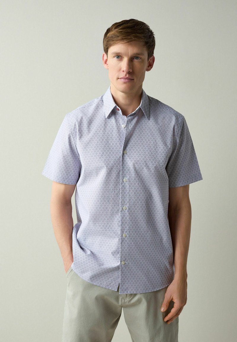 Chemise à manches courtes avec boutons en violet clair, motif géométrique, fabriquée en tissu respirant. Comprend un col rabattable et des boutons.