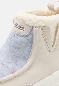 Beige ankelsko med overdel i ullblanding i nyanser av blått og lilla, foret med hvit faux pels, med Columbia-logoen.