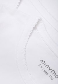 Weiße Baumwollhemden mit gewelltem Saum am Ausschnitt, auf denen der Markenname "minymo" und die Größenangaben in Grau aufgedruckt sind.