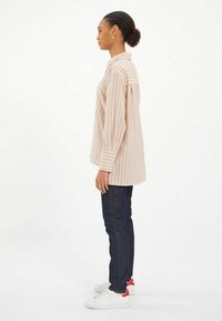 Chemise à manches longues rayée en beige et rose clair, avec un design droit. Associée à un jean noir et des baskets blanches avec des accents rouges.