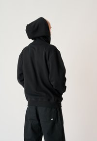Black hoodie made of soft fabric, featuring a large hood and relaxed fit, paired with black trousers with a subtle patch detail.