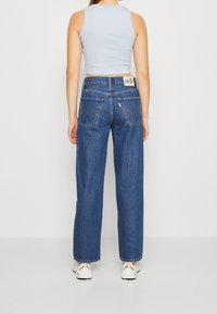 Modré džíny s vysokým pasem a rovnými nohavicemi, dvě zadní kapsy a kožená nášivka na pase. Texturovaná tkanina s mírným rozšířením na lemu.