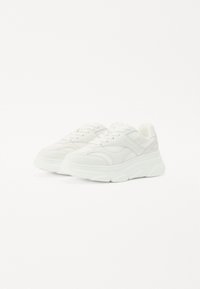 Zapatillas blancas con parte superior de malla, acentos texturizados y una suela de goma gruesa para mayor soporte y comodidad.