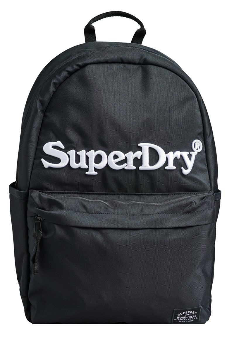 Zaino in tessuto nero con schienale imbottito, manico superiore, spallacci regolabili, tasca anteriore con zip e logo "SuperDry" bianco sul davanti.