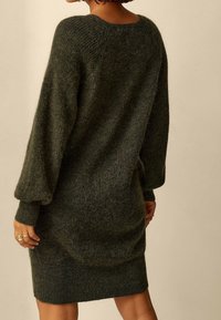 Abito lavorato a maglia verde scuro con una vestibilità rilassata, caratterizzato da maniche lunghe a sbuffo, scollo rotondo e polsini e orlo a costine. Tessuto morbido.