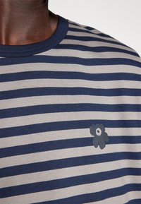 Camiseta de rayas en azul marino y gris claro con un escote redondo, textura de la tela visible, que presenta un pequeño gráfico de una flor impreso cerca del pecho.