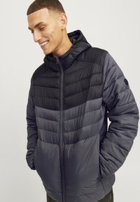 Padded hooded jacket in dark gray with a contrasting lighter gray striping pattern, featuring a front zipper and side pockets.