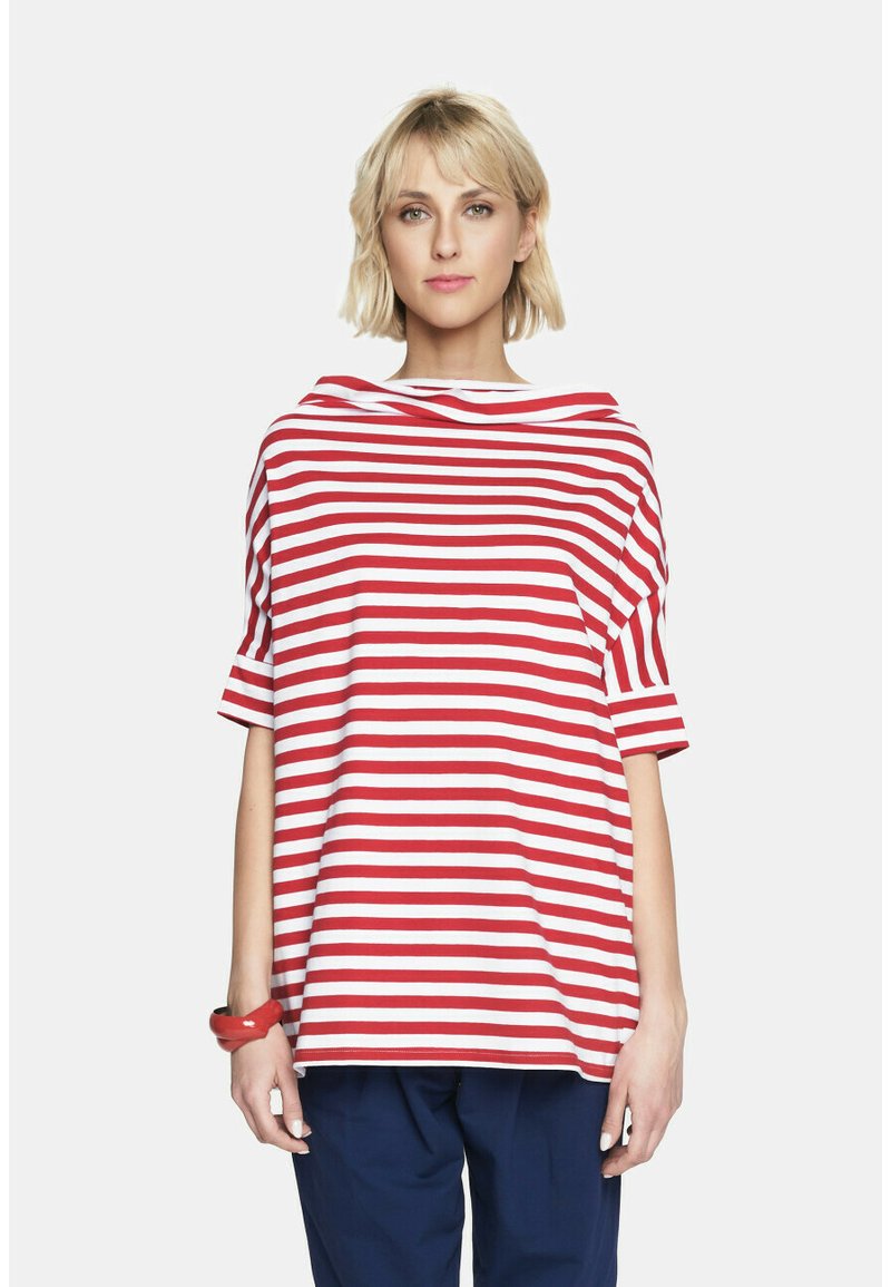 Czerwona i biała w pasiaki bluzka z krótkim rękawem i szerokim, luźno opadającym dekoltem. Luźny krój z miękkiego materiału, zestawiona z niebieskimi spodniami i czerwoną bransoletką.