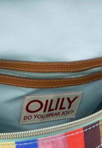 Intérieur d'un sac en tissu multicolore avec une doublure lisse et bleu clair, des finitions en cuir, et une étiquette blanche comportant le mot "OILY" en texte rouge.