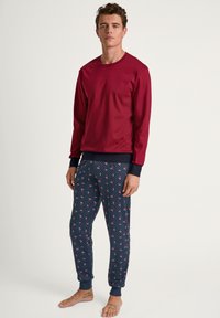 Maglietta rossa a maniche lunghe abbinata a pantaloni da pigiama blu navy con un piccolo motivo a pois bianchi e fiori di ciliegio rosa. Tessuto morbido, vestibilità rilassata.