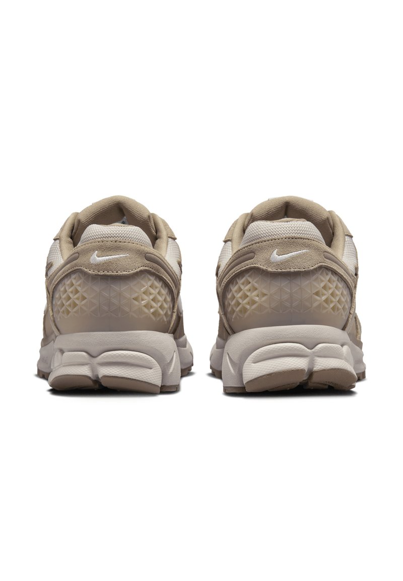 Zapatillas Nike en tonos beige, con materiales de malla y ante, un talón texturizado con patrón de diamante y una suela blanca acolchada.