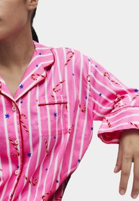 Różowe piżamy w paski z nadrukiem czerwonych lasek cukrowych i niebieskich gwiazdek. Koszula ma kieszeń i kontrastowy kołnierzyk z guzikami.