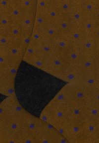 Braune Socken mit lila Pünktchen, ausgestattet mit einem schwarzen gerippten Bündchen. Das Material ist glatt und dehnbar, mit einer feinen Strickstruktur.