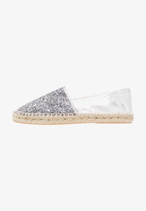 Espadrille plateado con parte superior brillosa y lateral metálico. Cuenta con una suela de yute trenzada, punta redondeada y diseño plano.