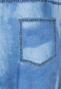 Tessuto di denim azzurro chiaro con tasca patch cucita con dettagli in filo giallo e blu scuro.