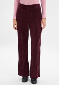 Bordeaux kleurige corduroy broek met verticale ribbels, vlakke voorkant en een aansluitende tailleband. Gecombineerd met donkere schoenen voor contrast.