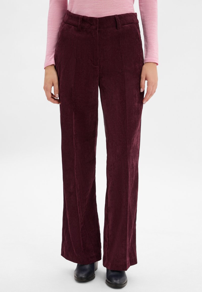 Bordeaux kleurige corduroy broek met verticale ribbels, vlakke voorkant en een aansluitende tailleband. Gecombineerd met donkere schoenen voor contrast.