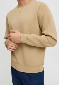 Beige bomulds sweatshirt med lange ærmer, ribbede manchetter og kant. Har en rund halsudskæring og diskret korsstingdetalje på kraven.
