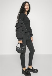 Μαύρο μπλουζάκι με μακριά μανίκια, σε συνδυασμό με μαύρα skinny τζιν και ογκώδεις μοκασίνες. Ένα μαύρο, καπιτονέ τσαντάκι κρατιέται στο ένα χέρι.