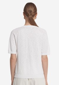 Vit strukturerad kortärmad tröja med rund hals, ribbade ärmslut och nederkant. Visar en lätt och avslappnad design.