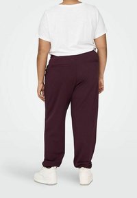 Burgundy joggers with side pockets and a relaxed fit, paired with a plain white t-shirt and white sneakers. Visible stitching detail.