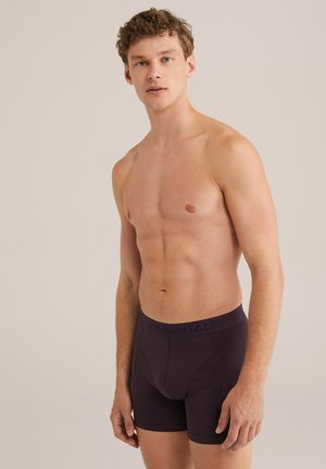Tumman violetit boxerit, jotka on valmistettu pehmeästä kankaasta. Samanmielinen leveä vyötärönauha, jossa lukee "FUNDAMENTALS", ja tiukka istuvuus.