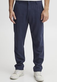 Pantaloni din in bleu marin cu o croială lejeră, prevăzuți cu închidere pe buton și buzunare laterale, asortați cu adidași albi.
