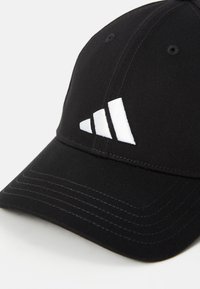 Fekete sapka textúrált anyagból, ívelt csúccsal, varrott részletekkel és kiemelkedő fehér Adidas logóval, három csíkkal.