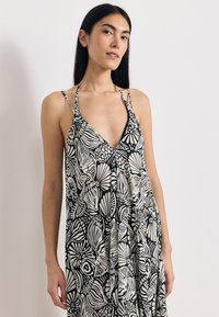 Φόρεμα με ασπρόμαυρο λουλουδένιο μοτίβο, βαθύ V-λαιμό και λεπτές τιράντες, με άνετη εφαρμογή και ρέουσα υφή υφάσματος.