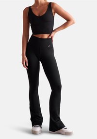 Top corto de canalé negro y leggings acampanados hechos de tela elástica. El top presenta un escote ancho; los leggings tienen una cinturilla alta y un detalle de logo.