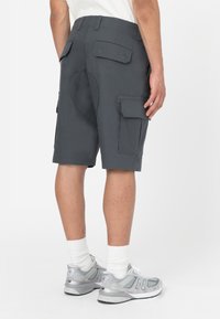 Shorts cargo gris avec plusieurs poches, une texture lisse et une taille ajustée. Portés avec des baskets grises et des chaussettes blanches.