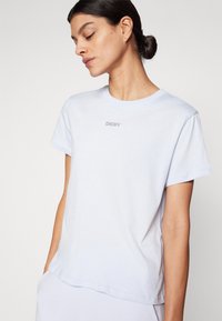 Šviesiai mėlynas medvilninis marškinėlis su apvalia iškirpte ir trumpomis rankovėmis. Priekyje yra mažas sidabrinis "DKNY" logotipas. Minkšta struktūra.