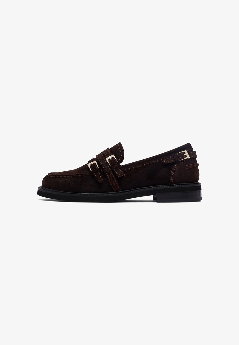 Braune Rauhleder-Loafer mit doppelten Riemen und silbernen Schnallenakzenten. Schwarze Gummisohle. Rundliche Zehenform und kontrastierende Nähte.