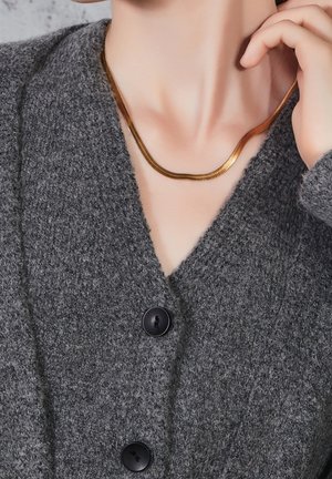 Collier en chaîne d'or sur une personne portant un pull boutonné gris foncé texturé, main reposant près du cou.