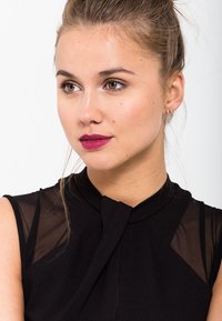 Haut sans manches noir avec des accents en maille transparents au niveau des épaules, présentant un col haut et un détail de plissé à l'avant.