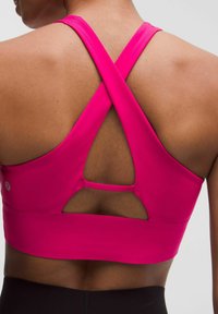 Sujetador deportivo fucsia con tirantes cruzados y detalle recortado en la parte posterior. Se observa una textura suave y un diseño ajustado.