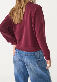Bordeaux sweatshirt met een ruime fit, geribbelde manchetten en taille. Gecombineerd met oversized lichtblauwe spijkerbroek met achterzakken.