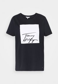Camiseta de algodón negra con cuello redondo, que presenta un gráfico cuadrado blanco con un logotipo manuscrito en negro en el centro. Mangas cortas.