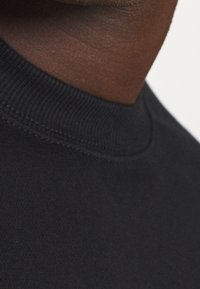 Prenda de cuello alto negra con cuello acanalado y textura lisa, mostrando detalles de costura y vista en primer plano de la tela.