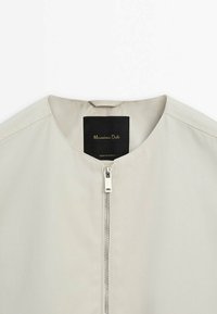 Beige letvægtjakke med rund halsudskæring, sølvfarvet lynlås foran og sort indvendig etiket med teksten "Massimo Dutti, Made in Portugal."