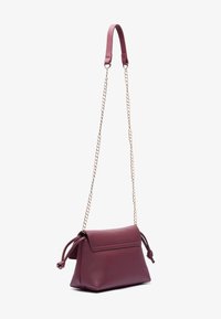Sac à épaule en cuir bordeaux avec une chaîne, détail de cordon noué et texture lisse ; forme structurée avec fermoir à rabat.