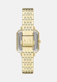 Pulsera de reloj en metal dorado con cierre rectangular grabado con "A|X Armani Exchange" y cara del reloj parcialmente visible detrás.