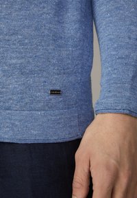 Pull bleu en maille avec une finition texturée, arborant un patch logo noir à l'ourlet ainsi que des poignets et une taille côtelés.